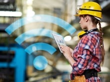 Woman in a hardhat working on a tablet computer in a factory with a blue wi-fi icon in the background