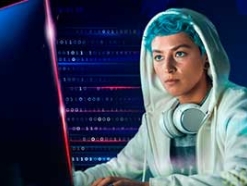 Blue-haired woman in a white hoodie looking at a monitor