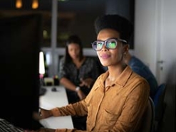 Mulher com óculos grandes e camisa marrom de mangas compridas trabalhando com um monitor 