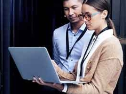 Man and woman in business attire and security lanyards looking at a laptop together